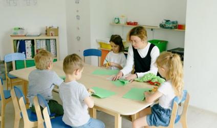 Teacher and young students sitting at a table folding and cutting green-colored construction papers