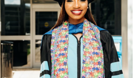 Dr. Lewis-Hunte smiling and posing in her full graduation garb outside of a university building