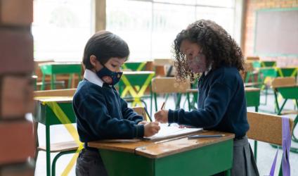[photo of two young students in school uniforms sitting at a desk and coloring]