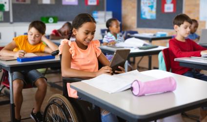 [image of a student in a wheelchair at a desk in a classroom using a computer tablet]