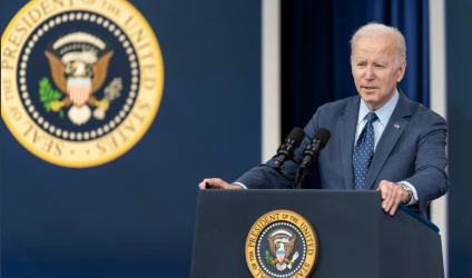 President Biden at a podium against a blue and black background with the President's seal