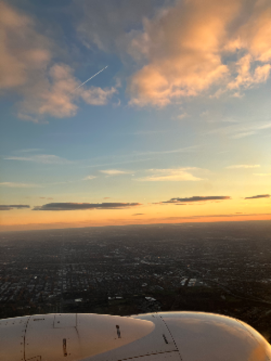 [image of the land and sky from an airplane window during sunset in mid-flight, with the plane engine included in the view] 