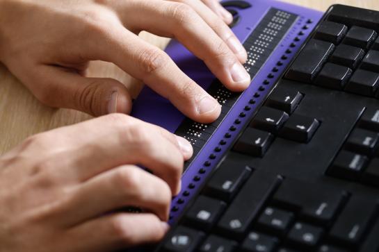 [image of a close up of hands typing on a braille keyboard next to a common keyboard] 