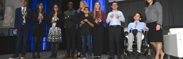 A group photo of the 2020 Yes I Can recipients smiling and posing on stage with their awards