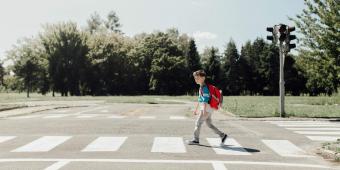 Young male student with a backpack walking across a school crosswalk